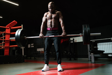 Male athlete or fitness trainer doing deadlift with a barbell in the gym