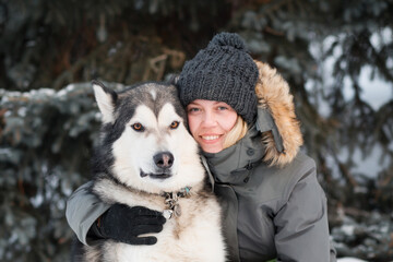 Happy woman embracing alaskan malamute in winter forest. close up.
