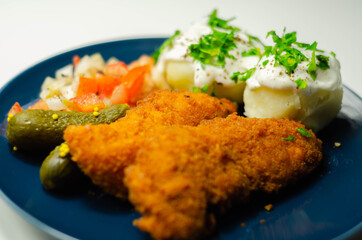 Breaded and herbed chicken breast fillet served with mashed potatoes,  tomato salad with onions and gherkin