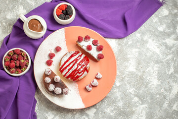 top view of plate of dessert on purple napkin with berries and chocolate on side on marble background