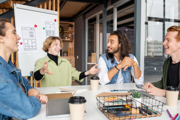 Young joyful businesswoman looking at one of male colleagues during discussion