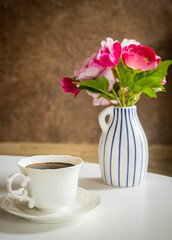 Obraz na płótnie Canvas A cup of black coffee on the table behind it a stylish pot with a bouquet of flowers