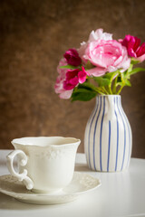 a stylish cup standing on the table and a jug with a bouquet of flowers