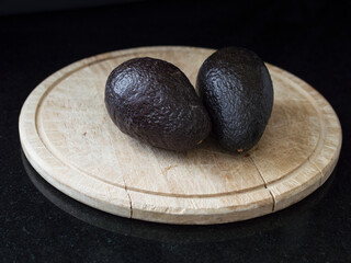 Two Avocado's on a wooden board with black background