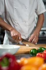 Hands of young male chef of restaurant chopping fresh vegetables on board