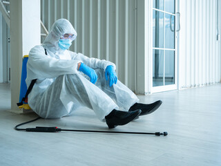 Asian cleaner man feel tired about Coronavirus or Covid-19 disease prevention from second wave pandemic although use sanitizer spray and wear safety uniform with face mask and blue gloves when service