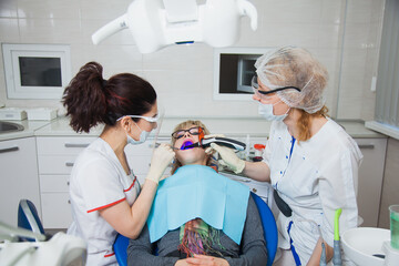 Closeup shot of dentist and assistant in protection mask working with tooth cavity and plague. Patient repair aching teeth. Stomatologist and patient at clinic office. Toothcare concept