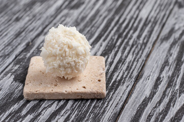 Round candy in coconut flakes on black wooden table.