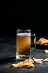 Beer is poured into a glass on a dark background. Potato chips for beer