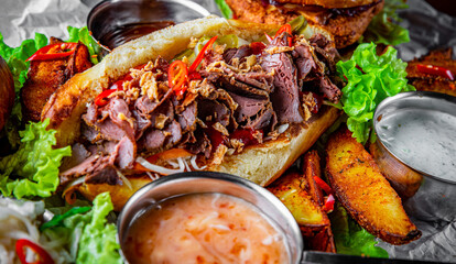 Philly cheese steak sandwich with meat, vegetables, cheese and sause on wooden table. street food