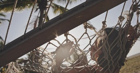 Asian woman relaxing during her summer vacation on tropical island under coco palms. Young girl on the beach, lying in a hammock and sun shining bright. Concept of lifestyle, relaxation and paradise