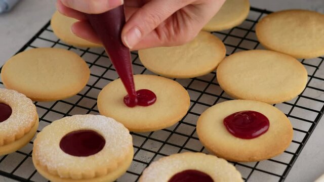 Female hands put jam on cookies from a pastry bag. Female hands a making homemade biscuit shortbread cookies with jam. Kurabye cookies with raspberry jam. Christmas cookies with jam.
