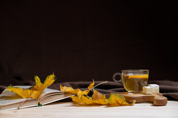 Autumn composition with an autumn yellow leaf and hot tea, sweets, cinnamon on a black background. Copy space, place for text. Cozy autumn