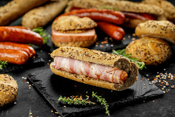 Still life composition of delicious hot dogs and sandwiches with different toppings and dried onion on the dark background