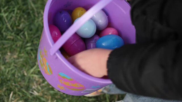Pink bucket full of plastic Easter eggs. Close up video of bucket with Easter eggs and hand picking them one by one.