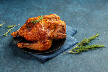 Still life concept with whole grilled chicken with golden brown crust, rosmary on a blue textured background with empty space