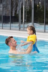 Happy young man lifting his cute little daughter while having fun in water