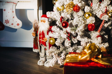 santa claus stands under a white christmas tree decorated with red balls