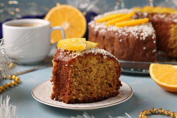 Homemade cake with oranges sprinkled with coconut flakes on a light blue background and cup of coffee. Piece of cake in the foreground. Closeup