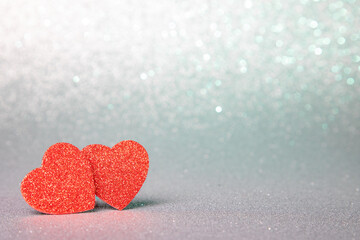two red hearts in glitter on a silver glitter background