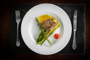 steak with asparagus served on a stone stand with buns and appliances