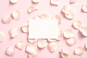 Fototapeta na wymiar Blank paper greeting card mockup and rose petals on pastel pink table. Happy Valentines Day, Mothers Day, birthday concept. Flat lay, top view.