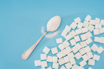 background of sugar cubes and sugar in a spoon. White sugar on a blue background. Sugar with copy...