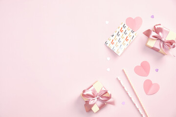 Valentines Day party concept. Gift boxes, greeting card, drinking straws, paper hearts, confetti on pink table. Flat lay, top view.