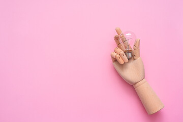 Light bulb in the toy wooden hand on the pink background with copy space.