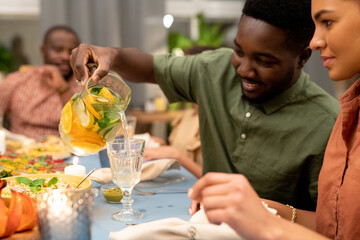 Happy African guy pouring fresh homemade lemonade into glass of his girlfriend