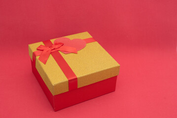 Gift box with golden lid and heart note on red background