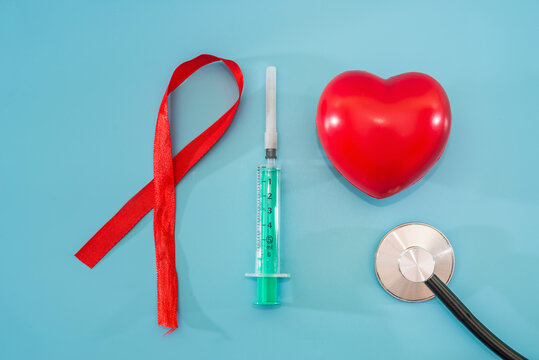 red ribbon, syringe and heart on blue background with copy space for text. World AIDS Day, healthcare and medical concept.