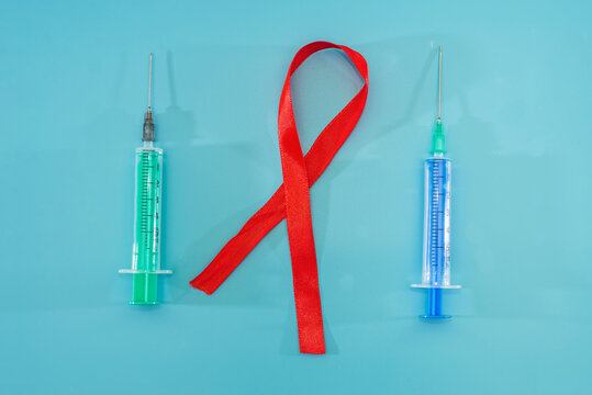 AIDS concept, red ribbon and syringes on blue background.
