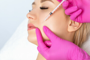 Cosmetologist makes rejuvenating anti wrinkle injections on the face of a beautiful woman. Female...