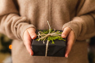 Womans hands holding nice present wrapped in black paper and decorated with green branch, close up