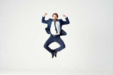 Energetic business man in a blue suit jumps up on a light background success joy emotions