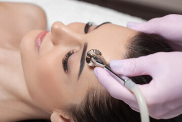 Fototapeta premium The cosmetologist makes the procedure Microdermabrasion of the face skin of a beautiful girl in a beauty salon.Cosmetology and professional skin care.
