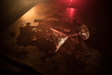 Broken glasses on wooden table at dark toned background with fog. Selective focus