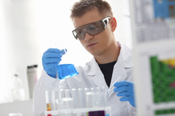 A male chemist holds test tube of glass in his hand overflows a liquid solution of potassium permanganate conducts an analysis reaction takes various versions of reagents using chemical manufacturing