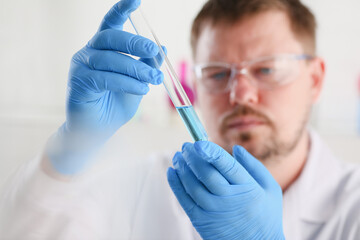 A male chemist holds test tube of glass in his hand overflows a liquid solution of potassium...