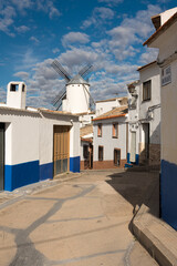 Cobbled street, white houses and windmills in the old town of Campo de Criptana on a day with blue sky and clouds, Ciudad Real, Spain