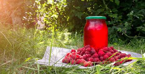 Raspberry drink in jar and ripe raspberry outside on green and sunlight background