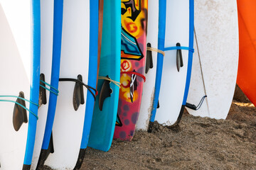 Close up many blue and white surfing longboard with surf fins and leash ready for rent in a stack by ocean. Surf lessons, water sport and adventure camp on summer vacation.