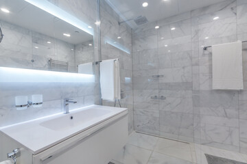 Beautiful modern bathroom with large backlit illuminated mirror, sink, and glass shower