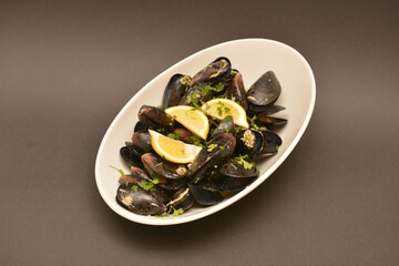 Black mussels on a white oval plate. Decorated with lemon wedges. Located on a black and white background. Can be used in the restaurant menu.