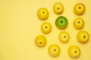 One green apple among the yellow. Apples on yellow background. Sweet and delicious fruits. One different among the like concept.