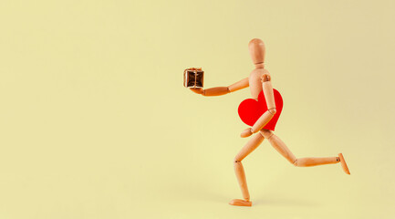 Fototapeta na wymiar A small wooden man runs and holds a heart in one hand and a gift in the other.