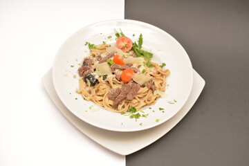Pasta with beef, prunes and parmesan cheese on a white plate. Located on a black and white background. Can be used in the restaurant menu.