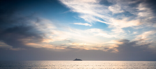 Sea with small island against cloudy sky