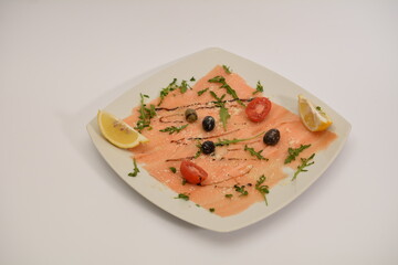 Salmon carpaccio on a white plate, decorated with tomatoes and herbs. A platter of Mediterranean cuisine. Can be used for restaurant menu.